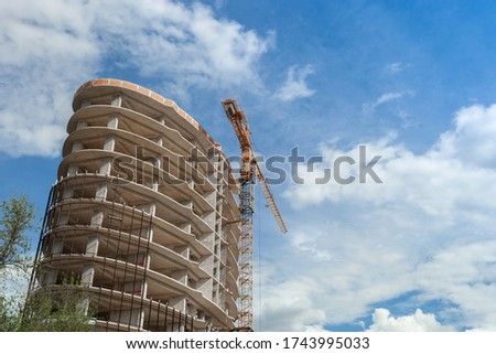 Multi-storey residential building under construction and crane on a background of blue sky