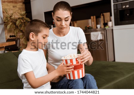 Mother and kid holding bucket with popcorn on couch at home