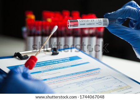 rt-PCR COVID-19 virus disease diagnostic test,lab technician wearing blue protective gloves holding test tube with swabbing stick,swab sample equipment kit and UK form specimen submitting guidelines