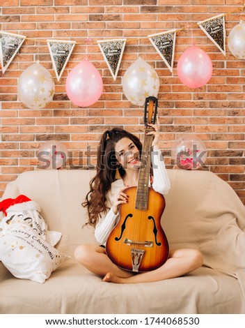 Stylish girl with a beautiful hairstyle sits on the bed with the guitar in her hands. The inscription on the triangular cards: "Happy Birthday"