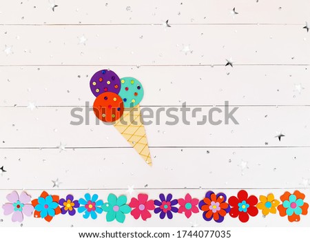 Composition of summer flowers, ice cream horn of multi-colored paper. Child make crafts his own hands. Cute DIY handmade art creativity on a wooden table with stars, sequins. Top view, copy space