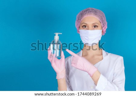 A doctor in a medical mask, cap and gloves points with his hands at the disinfectant on a blue background. The nurse is holding an antiseptic. Stop COVID-19. Copy space. Mock up