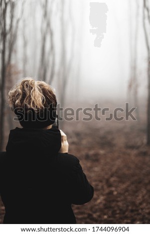 Young woman taking pictures with her mobile phone in a forest in autumn