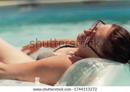 portrait of young beautiful woman hanging out on air mattress in above ground pool at home in yard.