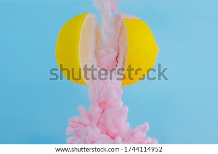 Partial focus of dissolving pink poster color in water drop between two slice lemons on blue background for summer, abstract and background concept.