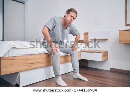 Tired adult male person leaning hands on the knees while going to stand up from bed