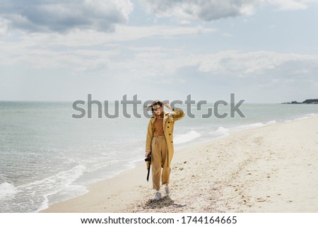 A young woman with a camera walks along the coast.
