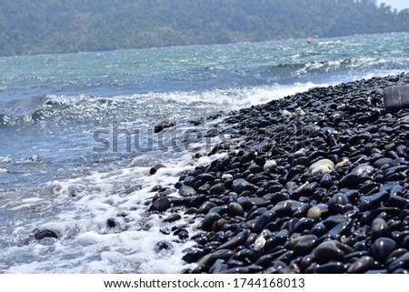 Sea picture impacting a black pebble beach. rock