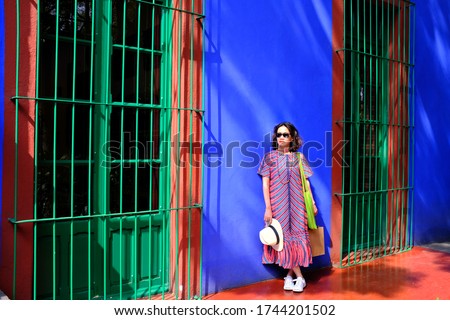 An Asian female tourist posing for a picture against the bright blue wall at Frida Kahlo Museum or Casa Azul in Coyoacán neighbourhood, Mexico City, Mexico.