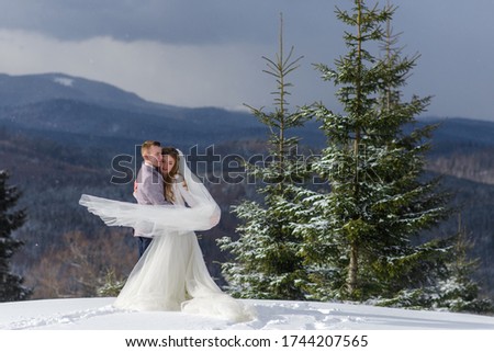 Groom hugs his bride against the backdrop of snow-capped mountains. Winter wedding photo.