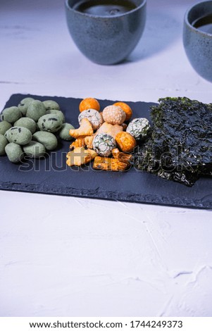 Asian snacks on a slate plate with green tea in background. Vertical picture.