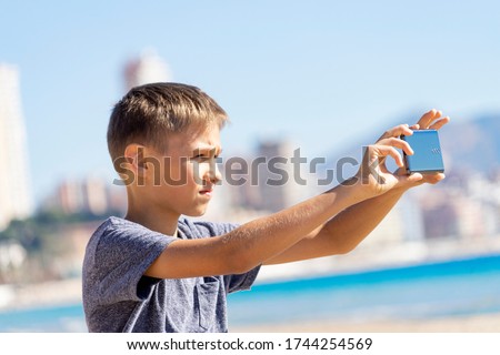 Boy taking photos using digital camera of mobile smartphone in city beach at sunny day