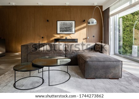 Stylish corner sofa with two modern coffee tables in living room with wooden and window walls
