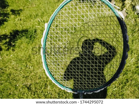 A man holds a tennis racket and photographs his silhouette, a shadow on green grass, meadow. Sports and recreation. Photography, concept.