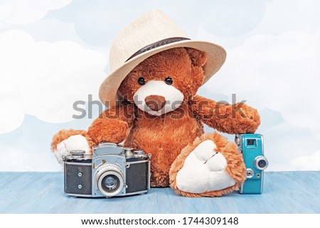 stuffed toy teddy bear in hat sitting and holds old photo camera and retro video camera on a blue sky background