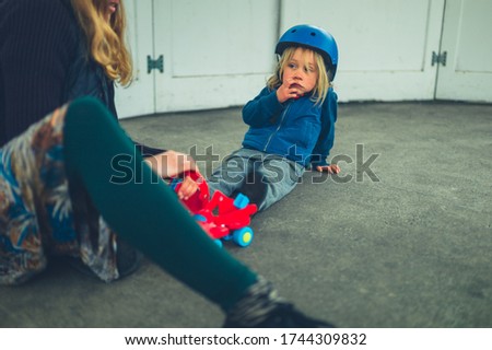A young mother is helping her preschooler put on his rollerskates