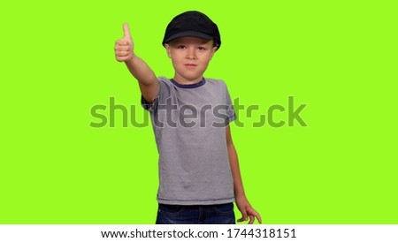 Little boy in black cap standing and showing thumb up sign on green screen background, Front view, Chroma key