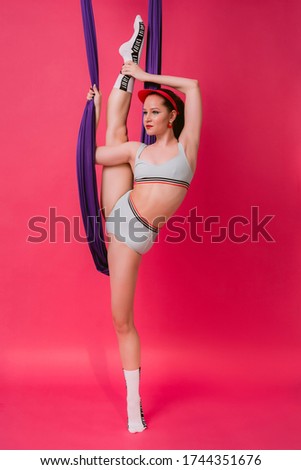 Full length body size view portrait cute pretty flexible sporty young womant gymnast in retro swim suit holds on air silk stretch out in splits over pink vivid background