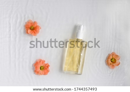 Glass,cosmetic bottle on white background with water and flowers. Top view, closeup