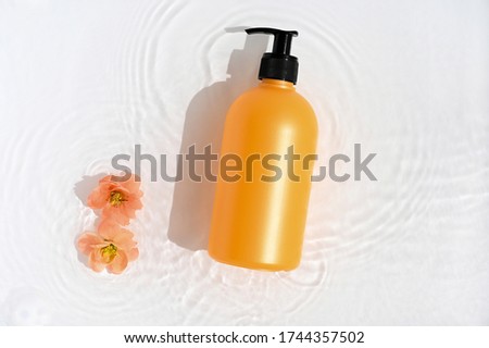 Cosmetic bottle on white background with water and flowers. Top view, closeup