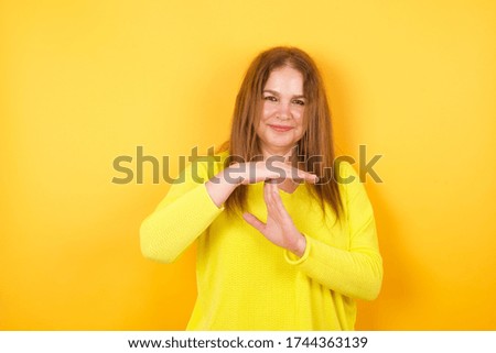 middle aged woman being upset against a yellow background showing a timeout gesture.
