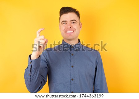 Young handsome Cucasian businessman wearing blue shirt standing against yellow background pointing up with fingers number nine in Chinese sign language Jiu