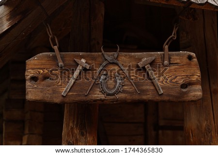 Old wooden signboard on a blacksmith's house. Forge, horseshoe, hammer