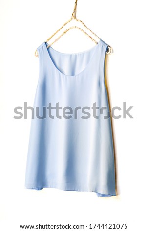 light blue tank top hanging on a hanger in a white wall.Close up