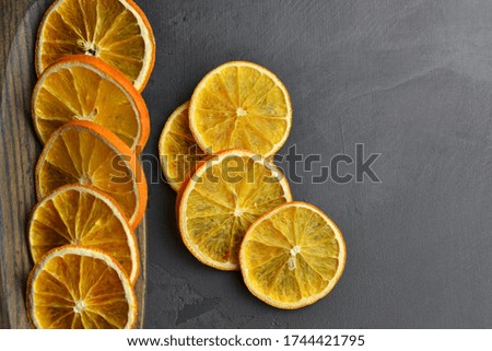 Dry orange slices in wooden plate on dark slate background