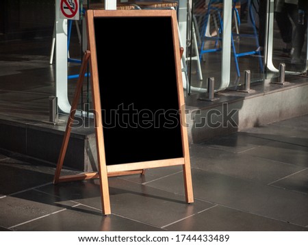 Blank outdoor advertising stand/sandwich chalkboard mockup template. Background texture of clear street signage board with wooden frame placed outdoor on pedestrian sidewalk near some dining seats.