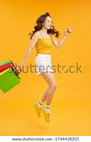 Joyful Teen Summer Girl Carrying Shopping Bags And Jumping In Air Over orange Background, Full-Length Shot With Copy Space