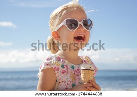 Adorable toddler girl eating ice cream. Portrait of child wearing sunglasses and holding an ice cream with beautiful blue sea and sky behind. Happy summer vacation on the beach. Royalty-Free Stock Photo #1744444688