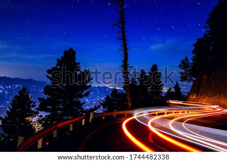 A Photograph With Curvy Road Light Trails And Star Trails As Well.
