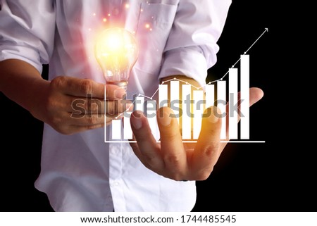 
The man in a white shirt stretched out with one hand holding a shining light bulb. And the other side holding white graphics,Creative concept with sparkling light bulbs and graphic white graph