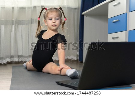 little girl sitting on a twine in front of a laptop at home. online stretching exercises