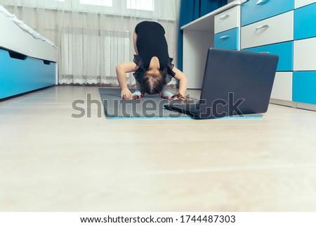the child does gymnastics on a gymnastic rug at home in front of a computer. sports distance learning. space for text, copy space