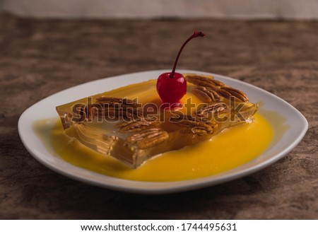 Detail of anise jelly with peach in syrup, walnut, eggnog and cherry in syrup dessert served on a white plate.