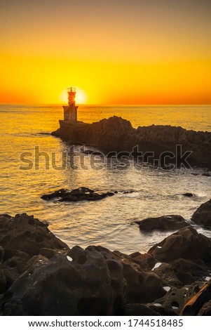 Detail of the sun behind the lighthouse in the orange sunset of the town of Pasajes San Juan. Gipuzkoa, Basque Country. Vertical photo