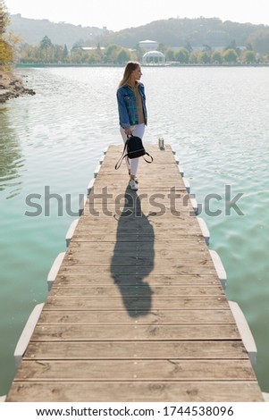 Beautiful woman walking on a pier on a lake on a background of rolling hills. Great photos from vacation and travel. Happy holiday.
