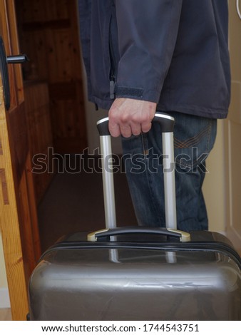 Man in black jacket holding handle of a travel case leaving the hotel room Travel concept.