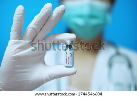 A female Asian physician with surgical mask and white rubber gloves at a clinic, holding a glass bottle of 1 dose PCV vaccine with white background and red letters. Royalty-Free Stock Photo #1744546604