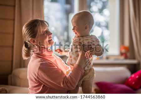 Grandmother is playing with her cute baby grand daughter in her country house. There are beautifully lighted dust particles in the air. Image with selective focus and toning.