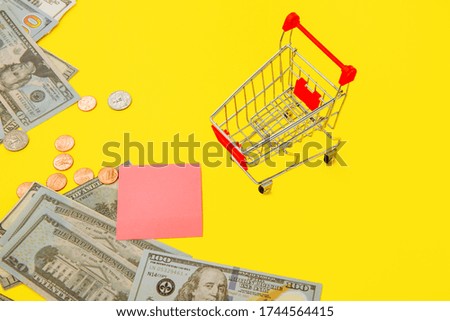 Shopping cart, money and space for text on yellow backgorund, concept for grocery expenses and consumerism