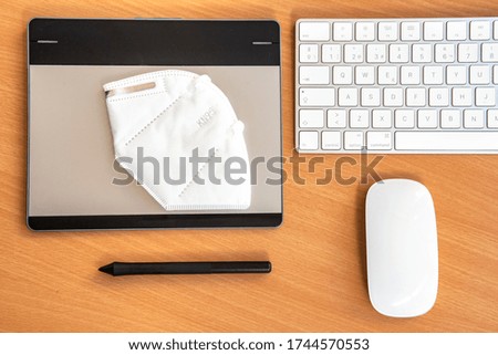 Computer keyboard, graphic design table, mouse and mask, with wooden background. 