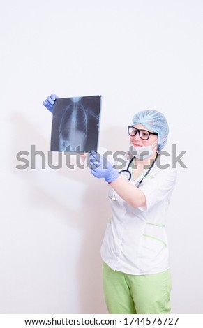 a doctor in a white coat, green trousers, protective mask, blue medical gloves, with a stethoscope around his neck, looking at a chest x-ray. on white background.