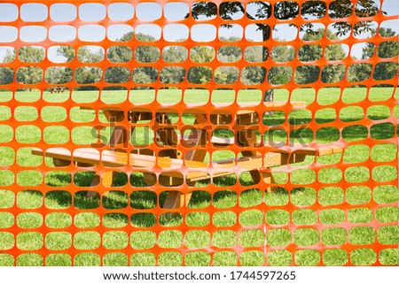 Closed picnic area with safety plastic orange grid against wooden picnic table on a green meadow - concept image.