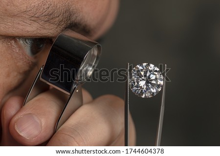 Close up male jeweller. Jeweller looking diamond though loupe. Cut and polished diamond. Big size diamond. Brilliant, magnifier, tweezers. Diamond expert. Royalty-Free Stock Photo #1744604378