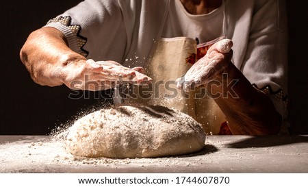 Woman great-grandmother clapping hands to dust a mound of freshly prepared pastry with flour dough for home baking. Royalty-Free Stock Photo #1744607870
