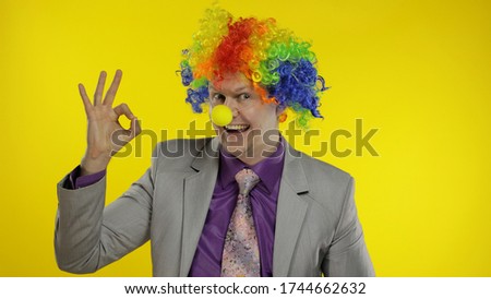 Successful clown manager office worker in wig and business suit at work show ok sign. Guy businessman entrepreneur boss smiles, looks at camera. Expressions. Chroma key. Halloween. Yellow background