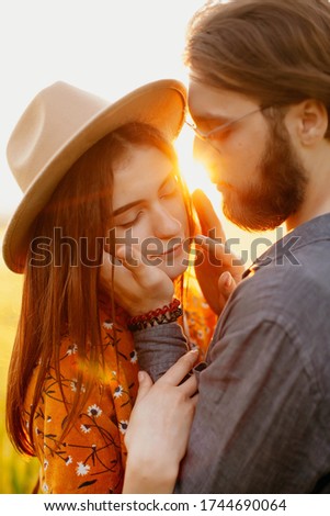 
young happy couple in a barley field at sunset. girl in a yellow dress and a guy with a beard. 
portrait of couple walking in the grass